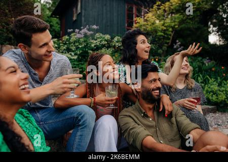 Glückliche männliche und weibliche Freunde mit Getränken, die Spaß auf der Gartenparty haben Stockfoto