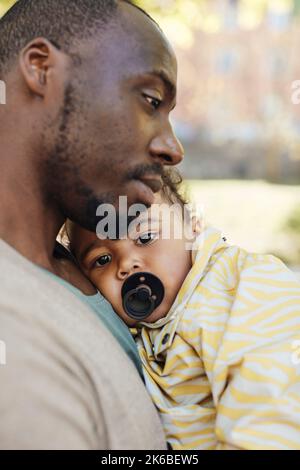 Porträt eines Kleinkindes mit Schnuller im Mund, der auf dem Vater ruht Stockfoto