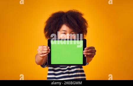Studio Portrait Of Boy Mit Digital Tablet Mit Grünem Bildschirm Gegen Gelben Hintergrund Stockfoto