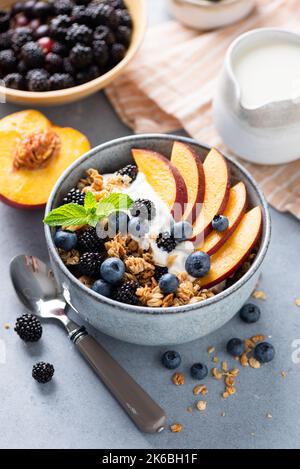 Frühstücksgranola Schüssel mit Joghurt, Pfirsich und Beeren. Gesundes, knuspriges Frühstückscerealien Stockfoto