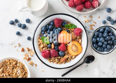 Müslischale mit Obst und Beeren auf weißem Marmorboden. Köstliche gesunde vegetarische Frühstückschüssel Stockfoto