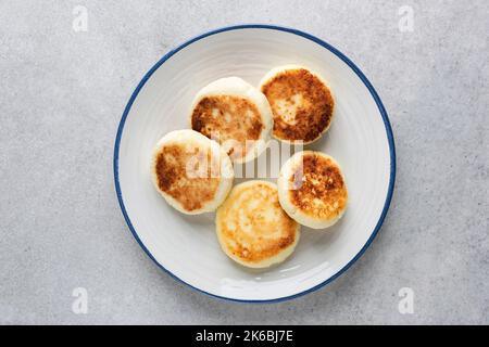 Quark-Krapfen Syrniki auf weißem Teller, Draufsicht. Grauer Betonhintergrund Stockfoto