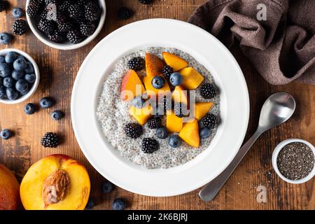 Chia Pudding Bowl mit Pfirsich und Heidelbeeren auf Holztisch Hintergrund, Draufsicht Stockfoto