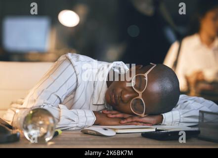 In meinen Träumen sind meine Arbeiten erledigt. Eine junge Geschäftsfrau schläft an ihrem Schreibtisch, während sie spät in einem modernen Büro arbeitet. Stockfoto