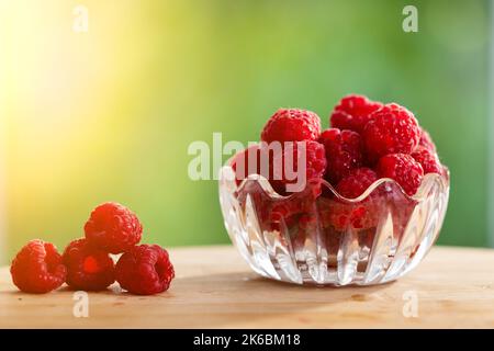 Nahaufnahme von frischen reifen Himbeeren in Glasschüssel auf Tisch mit grünem Hintergrund. Bio-Obst und gesunde Ernährung Konzept Stockfoto