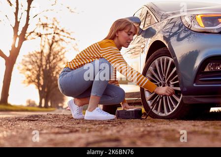 Frau, Die Autoreifen Mit Elektrischer Pumpe Auf Der Landstraße Aufpumpt Stockfoto