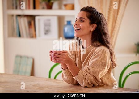 Frau, Die Sich Zu Hause Entspannt Und Am Tisch Mit Einem Heißen Getränk Sitzt Stockfoto