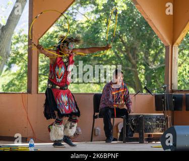 Navajo Native American Hoop Dancer in Regalia, die auf einem Festival in Moab, Utah, auftreten. Dahinter ç ein Schlagzeuger des Sängers. Stockfoto