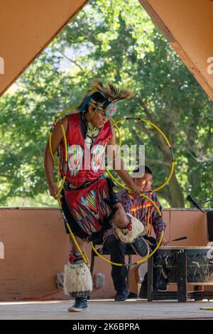 Navajo Native American Hoop Dancer in Regalia, die auf einem Festival in Moab, Utah, auftreten. Dahinter ç ein Schlagzeuger des Sängers. Stockfoto