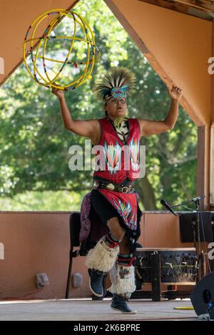 Navajo Native American Hoop Dancer in Regalia, die auf einem Festival in Moab, Utah, auftreten. Dahinter ç ein Schlagzeuger des Sängers. Stockfoto