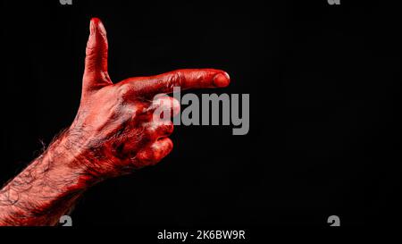 Blutige männliche Hand zeigt eine Waffe vor schwarzem Hintergrund. Stockfoto