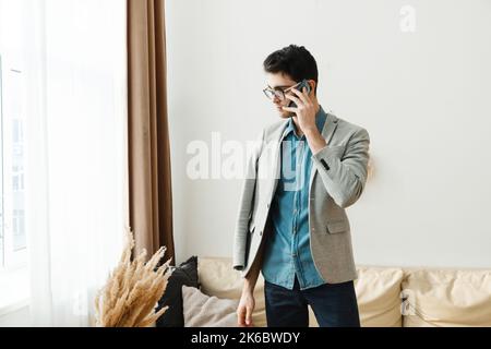 Ein junger ernsthafter Mann wird zu Hause arbeiten und telefoniert über Probleme Stockfoto