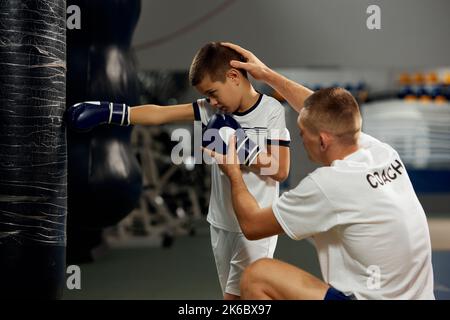 Training in Boxtechniken. Männlicher Junior-Boxer, der mit einem persönlichen Trainer im Sportstudio trainiert, innen. Konzept des Studierens, Herausforderungen, Sport Stockfoto