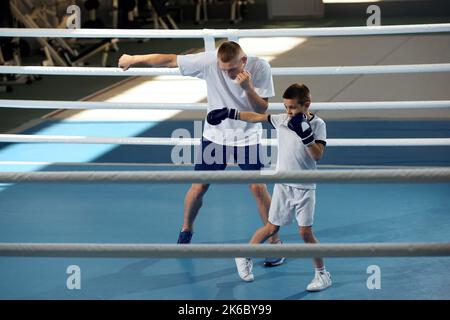 Training in Boxtechniken. Männlicher Junior-Boxer, der mit einem persönlichen Trainer im Sportstudio trainiert, innen. Konzept des Studierens, Herausforderungen, Sport Stockfoto