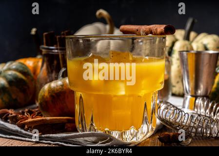 Hausgemachter alkoholischer Kürbis-Zimt-Cocktail, erfrischender eisgekühlter Kürbis-Gewürz-altmodischer Cocktail, Holzküchentisch im Hintergrund Kopierraum Stockfoto