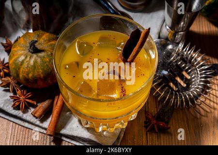 Hausgemachter alkoholischer Kürbis-Zimt-Cocktail, erfrischender eisgekühlter Kürbis-Gewürz-altmodischer Cocktail, Holzküchentisch im Hintergrund Kopierraum Stockfoto