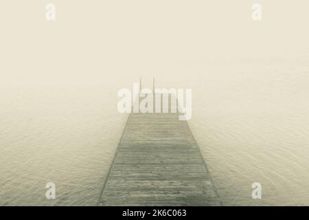 Traumhaftes Bild von einem hölzernen Steg auf dem See im Nebel Stockfoto