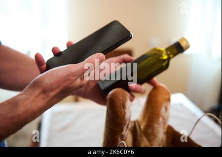 Scannen von QR-Codes mit dem Smartphone. Nahaufnahme Mann überprüft die Nährstoffe des Olivenöls auf einem Smartphone durch Scannen eines Barcodes Stockfoto
