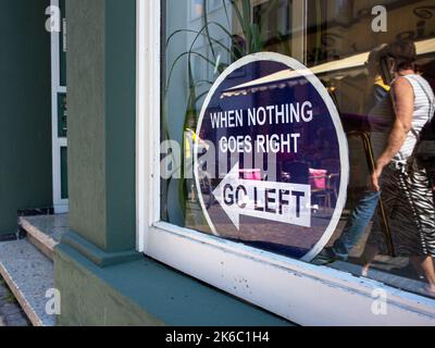 Schaufenster mit der Aufschrift: 'Wenn nichts nach rechts geht, nach links gehen'. Wenn Nichts Geht, Gehen Sie Nach Links. Menschen In Der Reflexion, Die In Die Richtung Gehen Stockfoto