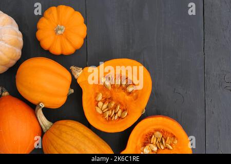 Kürbisse in der Küche. Orangefarbener Hokkaido-Kürbis mit Samen auf schwarzem Holzhintergrund schneiden. Stockfoto