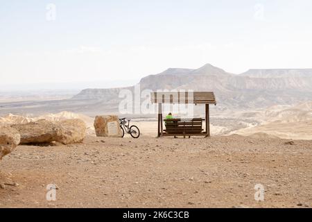 Biker, der sich auf einer Bank in einem Gedenkort ruht, mit Blick auf die wunderschöne Aussicht, die Negev-Wüste, Israel Stockfoto