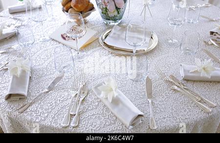 Brautmise en Place mit weißer Tischdecke aus Spitze und silbernem Besteck. Stockfoto