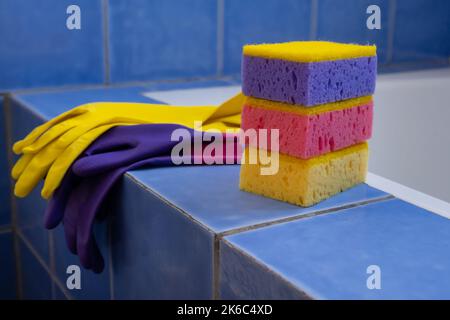 Gummihandschuhe und Schwämme im Badezimmer, Nahaufnahme. Set aus farbenfrohem Accessoire für die Hausreinigung. Sauberes Haus. Vorderansicht Stockfoto