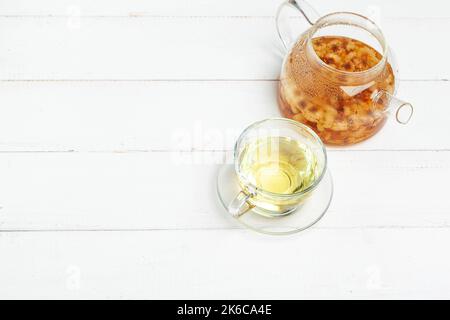 Glaskessel und Tasse Kräutertee auf weißem Holzhintergrund Stockfoto