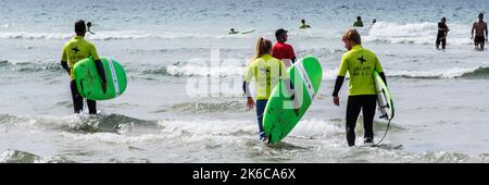 Ein Panoramabild von Urlaubern, die an einem Surfkurs mit einem Lehrer am Fistral Beach in Newquay in Cornwall in Großbritannien teilnehmen. Stockfoto