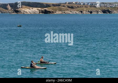 Zwei Urlauber sitzen auf Stand Up Paddleboards in Newquay Bay in Cornwall in England im Vereinigten Königreich. Stockfoto