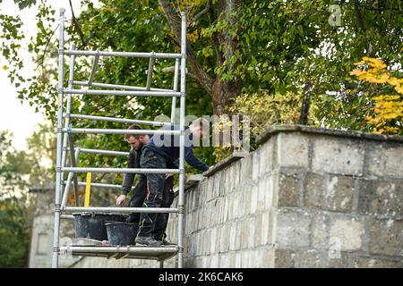 Oranienburg, Deutschland. 13. Oktober 2022. Während der Projektwoche "Lernen und Arbeiten" im KZ Sachsenhausen sind Kait (r) und Daniel mit Mauerarbeiten an der Lagermauer beschäftigt. 44 Auszubildende aus Bremen und Hennigsdorf lernen und arbeiten eine Woche lang in der Gedenkstätte und im Museum Sachsenhausen. Die angehenden Handwerker führen Renovierungsarbeiten durch und lernen die Geschichte des Konzentrationslagers (1936 bis 1945) und des sowjetischen Sonderlagers (1945 bis 1950) kennen. Quelle: Jens Kalaene/dpa/ZB/dpa/Alamy Live News Stockfoto