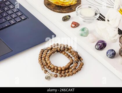 Laptop, Rosenkranz, Chakra-Steine, Duftstäbchen, Kerze auf Arbeitstisch Stockfoto