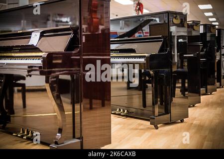 Eine Reihe von brandneuen, glänzenden, schwarzen Klavieren in einem Musikgeschäft Stockfoto