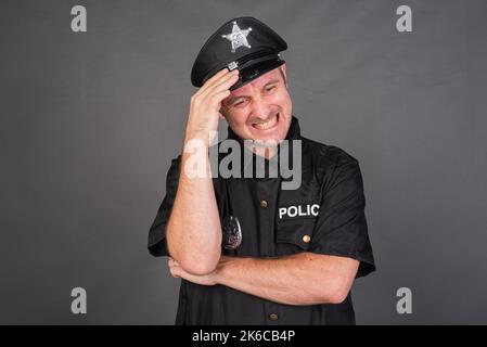 Frustrierter kaukasischer Mann mit Polizeiuniform-Kostüm vor grauem Studiohintergrund Stockfoto