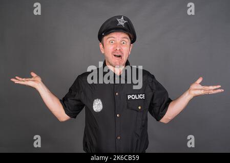 Frustrierter kaukasischer Mann mit Polizeiuniform-Kostüm vor grauem Studiohintergrund Stockfoto