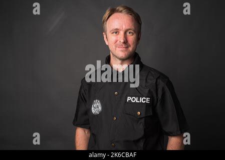 Porträt eines kaukasischen Mannes mit Polizeiuniform Kostüm auf grauem Studiohintergrund Stockfoto