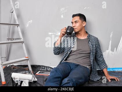 Ein junger asiatischer Mann nippt Kaffee, während er eine Pause vom Heimwerker nimmt Stockfoto