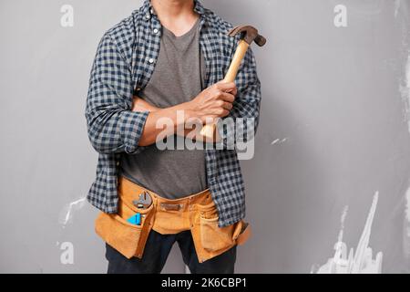 Ausgeschnittene Aufnahme eines Mannes, der Hammer hält und Werkzeuggürtel trägt, der für den Heimwerker bereit ist Stockfoto