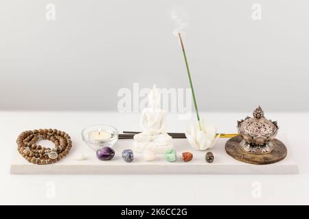 Rosenkranz-Perlen, Aromaschale, Duftstäbchen, buddha-Figur, Chakra-Steine und Kerze Stockfoto