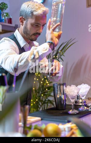 Der Barkeeper macht im Nachtclub einen Cocktail aus Mojito und fügt Zutaten hinzu und kreiert an der Theke Expertengetränke. Vertikale Aufnahme. Stockfoto