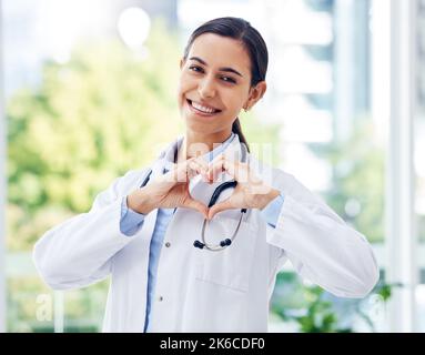 Ein guter Arzt zu sein bedeutet, unglaublich mitfühlend zu sein. Porträt einer jungen Ärztin, die mit ihren Händen eine Herzform in einem Krankenhaus macht. Stockfoto