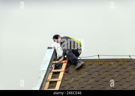 Der Reparaturleiter klettert eine Leiter hoch, während er das Dach repariert Stockfoto