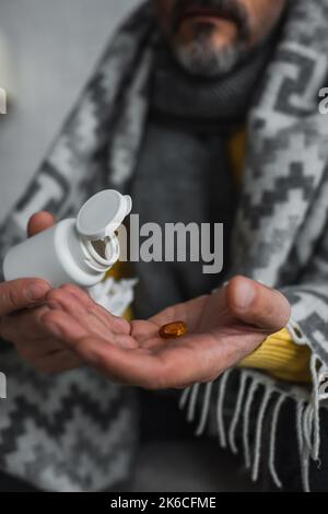 Beschnittene Ansicht des erkrankten Mannes, der Behälter und Pille auf verschwommenem Hintergrund hält, Stockbild Stockfoto