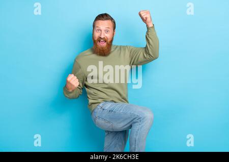 Portrait von guten Laune Kerl mit Ingwer Frisur tragen khaki Pullover schreiend yeah heben Fäuste isoliert auf türkisfarbenem Hintergrund Stockfoto