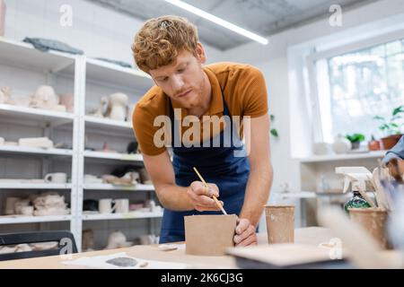 Bärtiger Mann in Schürze hält Shaper während der Töpferei-Klasse, Stockbild Stockfoto