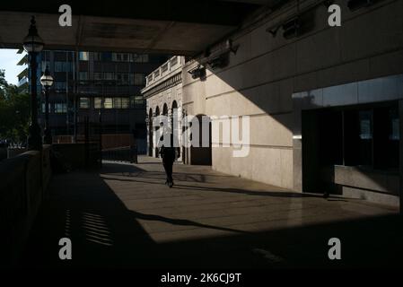 Ein Mann geht in Silhouette an der London Bridge Wharf unter der London Bridge, gefangen in der kontrastreichen Abendsonne. Stockfoto