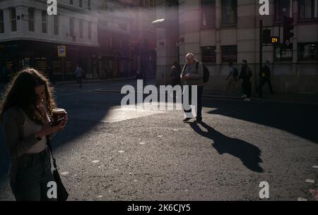 Mitglieder der Öffentlichkeit abgelenkt durch ihre Handys, warum zu Fuß über Straße in London im Abendlicht. Stockfoto