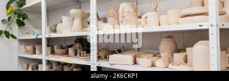 Verschiedene Tonskulpturen in der Nähe von Tassen und Schalen auf Regalen von Töpferei, Banner, Stockbild Stockfoto
