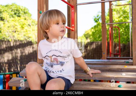 Ein Kind klettert an einem heißen Sommertag in einem Park auf einem Spielplatz auf ein alpines Netz. Kinderspielplatz in einem öffentlichen Park, Unterhaltung und Erholung f Stockfoto