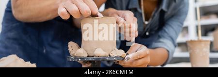 Beschnittene Ansicht des Mannes, der Tonskulptur in der Nähe afroamerikanischer Handwerker in Töpferwerkstatt, Banner, Stockbild macht Stockfoto